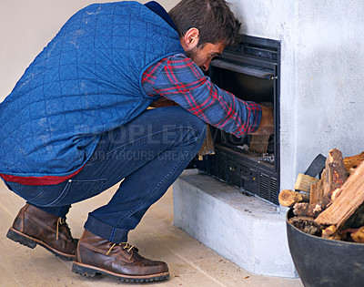 Buy stock photo Shot of a young man building a fire in his fireplace at home