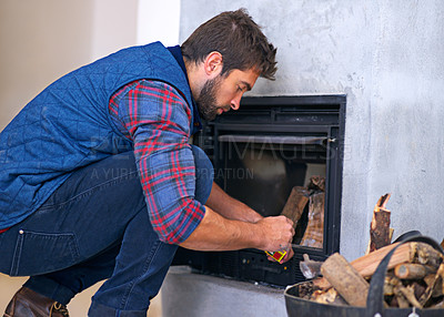Buy stock photo Shot of a young man building a fire in his fireplace at home