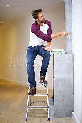 Buy stock photo Photo of an attractive young man painting a wall indoors while sitting on a ladder