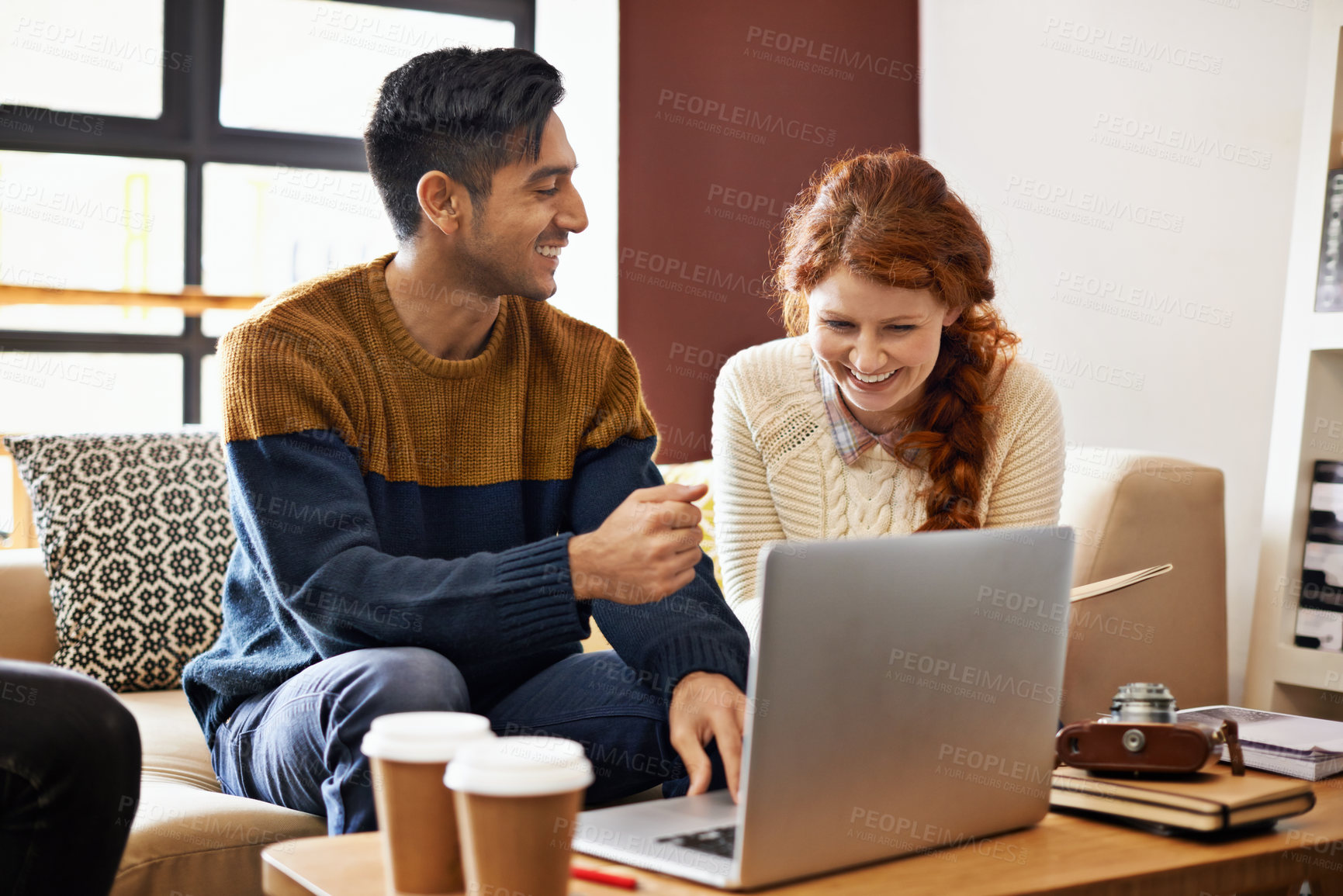 Buy stock photo Cropped shot of a young couple sitting on their laptop at a coffee shop