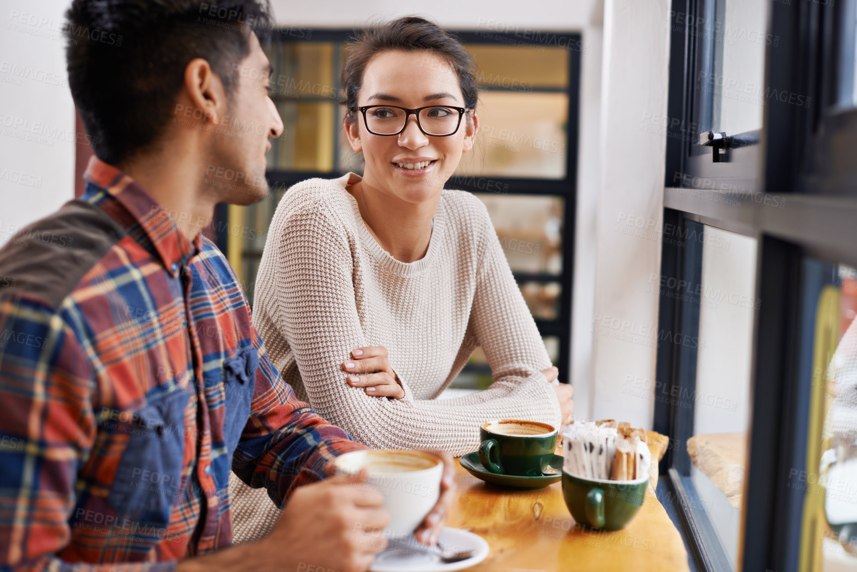 Buy stock photo Happy couple, window and relax with coffee at cafe for chatting, talking or social bonding. Young man and woman with smile for conversation, beverage or morning drink at indoor restaurant together