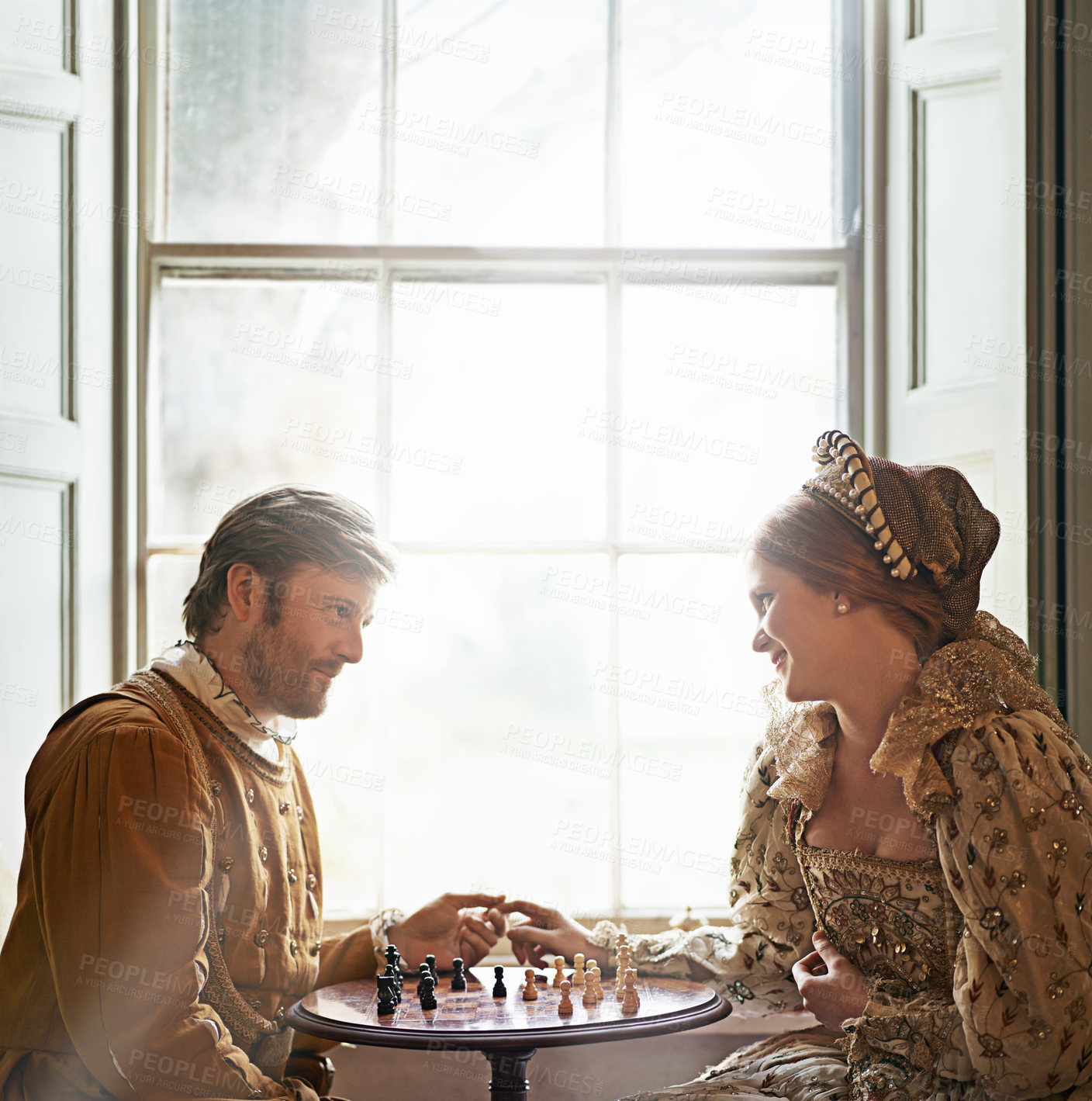 Buy stock photo Renaissance, couple and chess date in home with holding hands, vintage and medieval costume in a palace. Window, luxury and queen together with smile from strategy game and talking with love and care