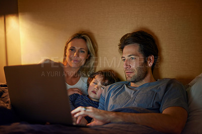 Buy stock photo A young family lying in bed and looking at a laptop screen