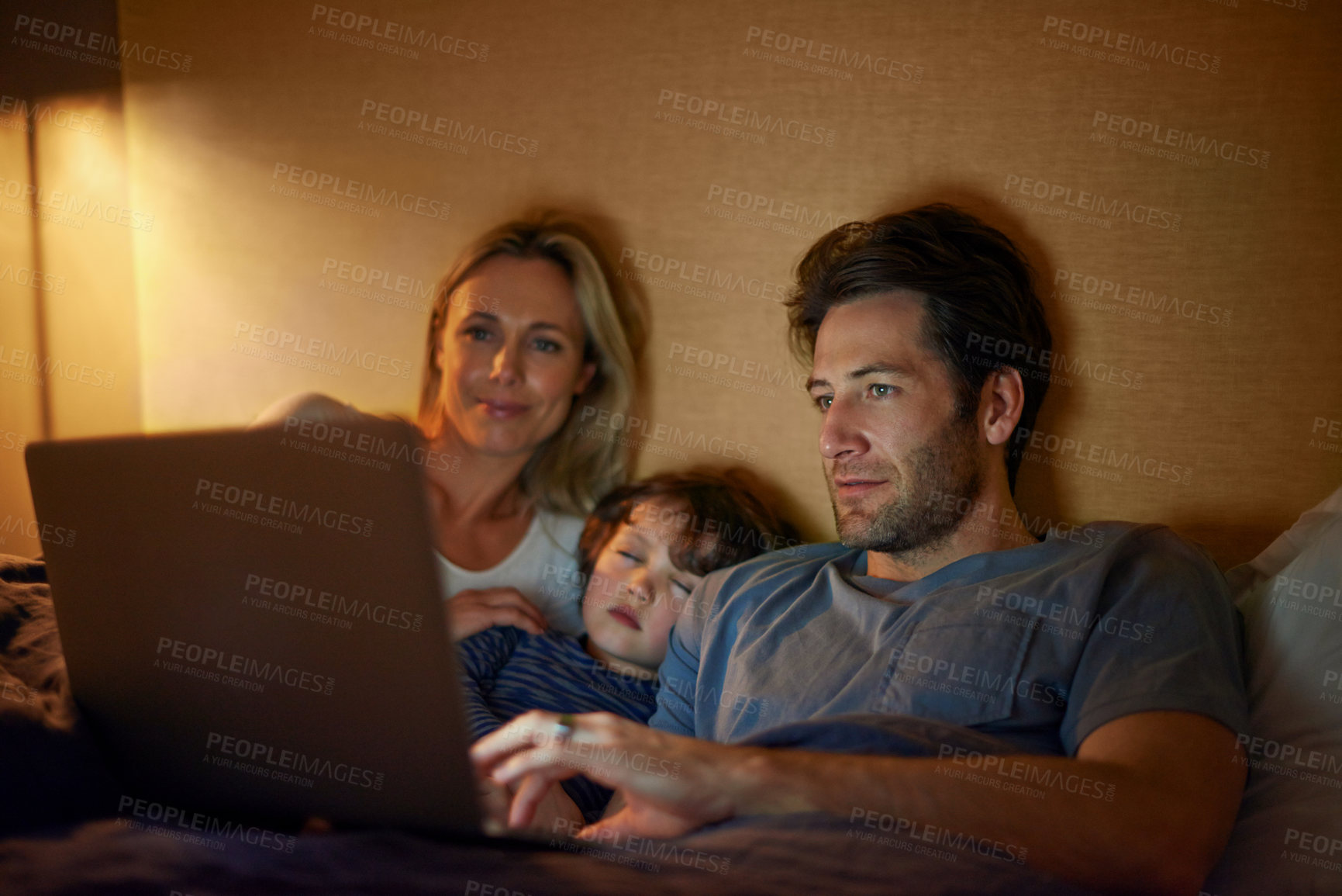 Buy stock photo A young family lying in bed and looking at a laptop screen