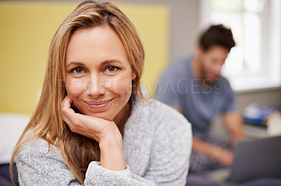 Buy stock photo Smile, portrait and woman on bed in home with husband work on laptop for remote freelancer job. Happy, couple and female person with positive attitude in bedroom with man typing on computer at house.