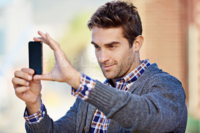 Buy stock photo Shot of a handsome young man taking a photograph with his mobile phone phone outdoors