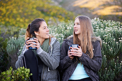 Buy stock photo Shot of two attractive young women enjoying hot drinks while out hiking