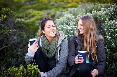 Buy stock photo Shot of two attractive young women enjoying hot drinks while out hiking