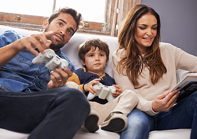 Buy stock photo Shot of a son and his father playing a video game together while his mother reads a magazine
