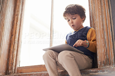 Buy stock photo Home, tablet and serious kid on app, internet and typing for learning game by windowsill. Technology, child and boy in house for education, scroll and watch cartoon online on digital electronics