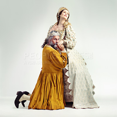 Buy stock photo King, queen and kiss hand in studio for love, romance and bonding in drama, theatre or renaissance. Ancient royal couple, man kneeling and sorry with romantic gesture, holding hands and background