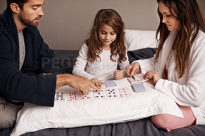 Buy stock photo Parents, girl and game of cards in home with bonding, learning and relax with strategy in bedroom. Father, mother and daughter with deal, playing and teaching on bed with connection in family house