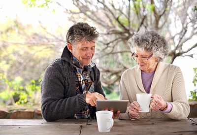 Buy stock photo Shot of a senior couple using a digital tablet while having coffee