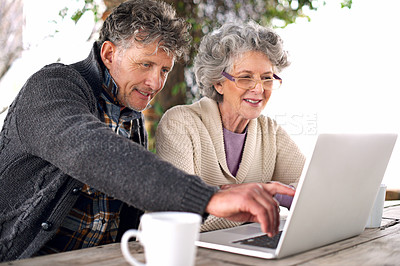 Buy stock photo Shot of a senior couple using a laptop at an outside table