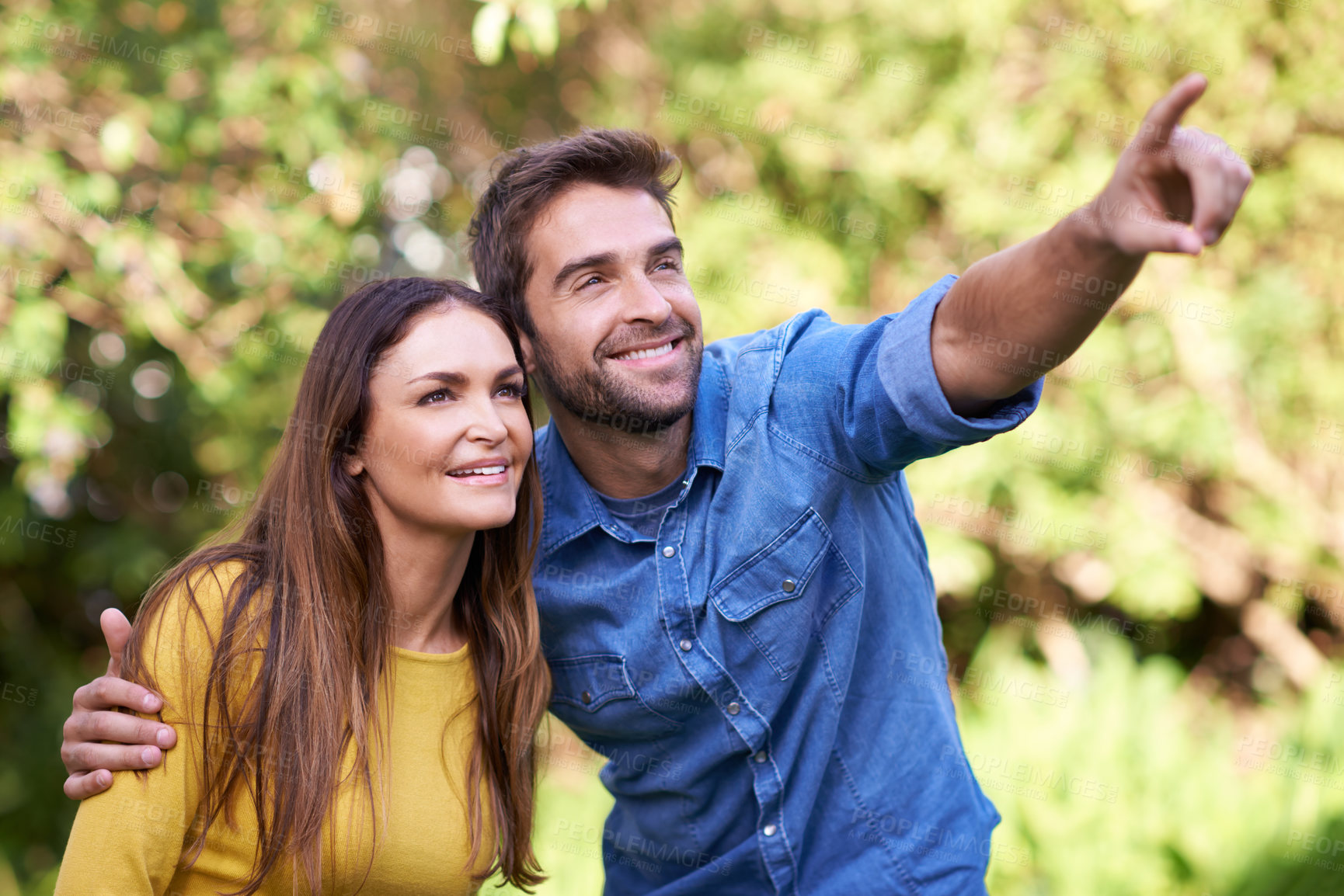 Buy stock photo Happy couple, women and man pointing in nature or park for bonding, dating and relationship with smile. People, love and romantic in backyard or outdoor with joy, excited and commitment in marriage