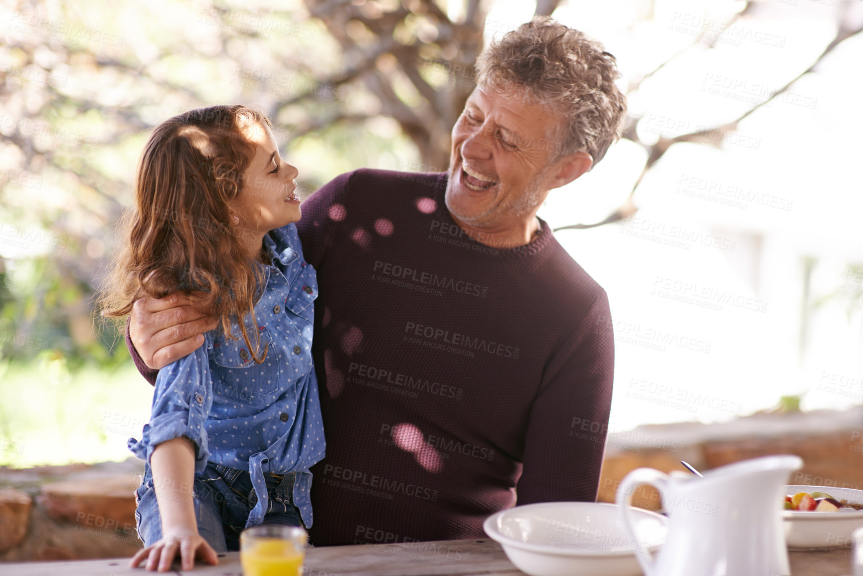 Buy stock photo Shot of a little girl and her grandfather having breakfast together outside