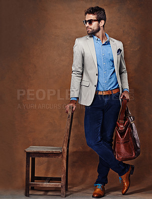 Buy stock photo Bag, chair and man with suit for fashion, style and formal wear isolated on studio background. Male person, gentleman and businessman with trendy clothes, class and outfit in brown backdrop
