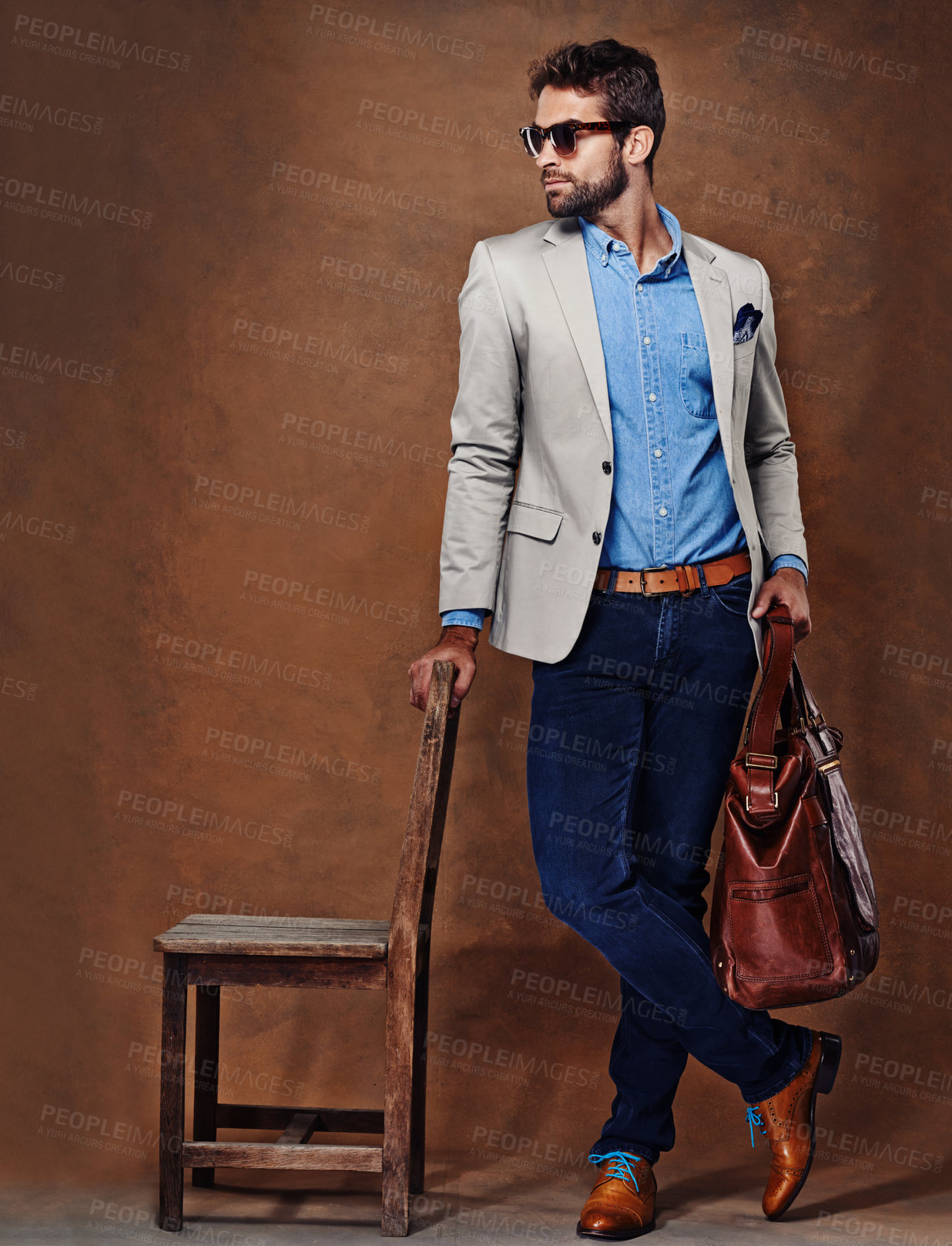 Buy stock photo Bag, chair and man with suit for fashion, style and formal wear isolated on studio background. Male person, gentleman and businessman with trendy clothes, class and outfit in brown backdrop
