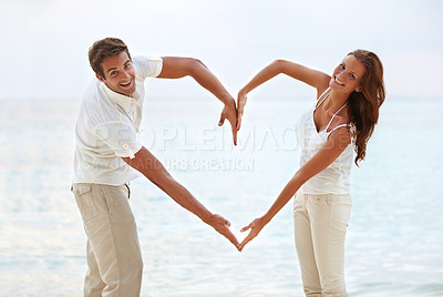 Buy stock photo couple, and heart sign with arms by beach for love, affection and support for relationship. Happy, man and woman with emoji for trust, marriage and commitment on outdoor holiday or summer vacation