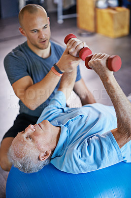 Buy stock photo Physiotherapist, dumbbell and old man on exercise ball for osteoporosis treatment in fitness centre, workout and pain reduction for elderly person. Male retiree, professional and senior care. 