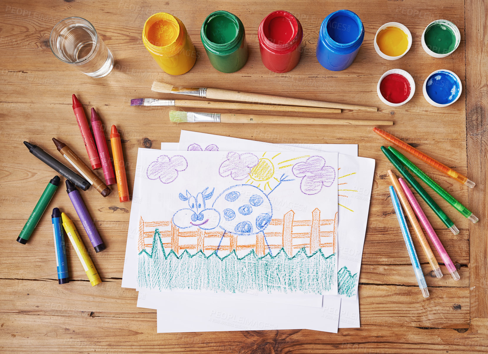 Buy stock photo Art, painting and creative supplies on a wooden desk with a drawing on paper from above. Paintbrushes, colors and still life containers ready to create artwork in school or class for education