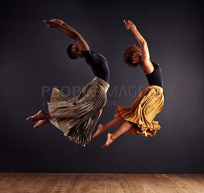 Buy stock photo Two contemporary dancers performing a synchronized leap in front of a dark background