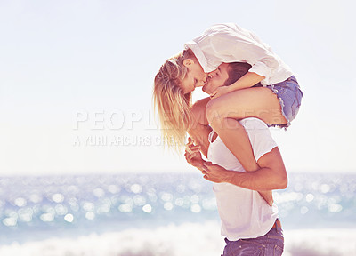 Buy stock photo Couple, piggyback and kiss with love on beach, holiday or vacation together with playful game or bonding. Summer, date and man support woman on back with care at sea, ocean and relax in nature 