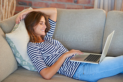 Buy stock photo Shot of a young woman using a laptop on her sofa at home