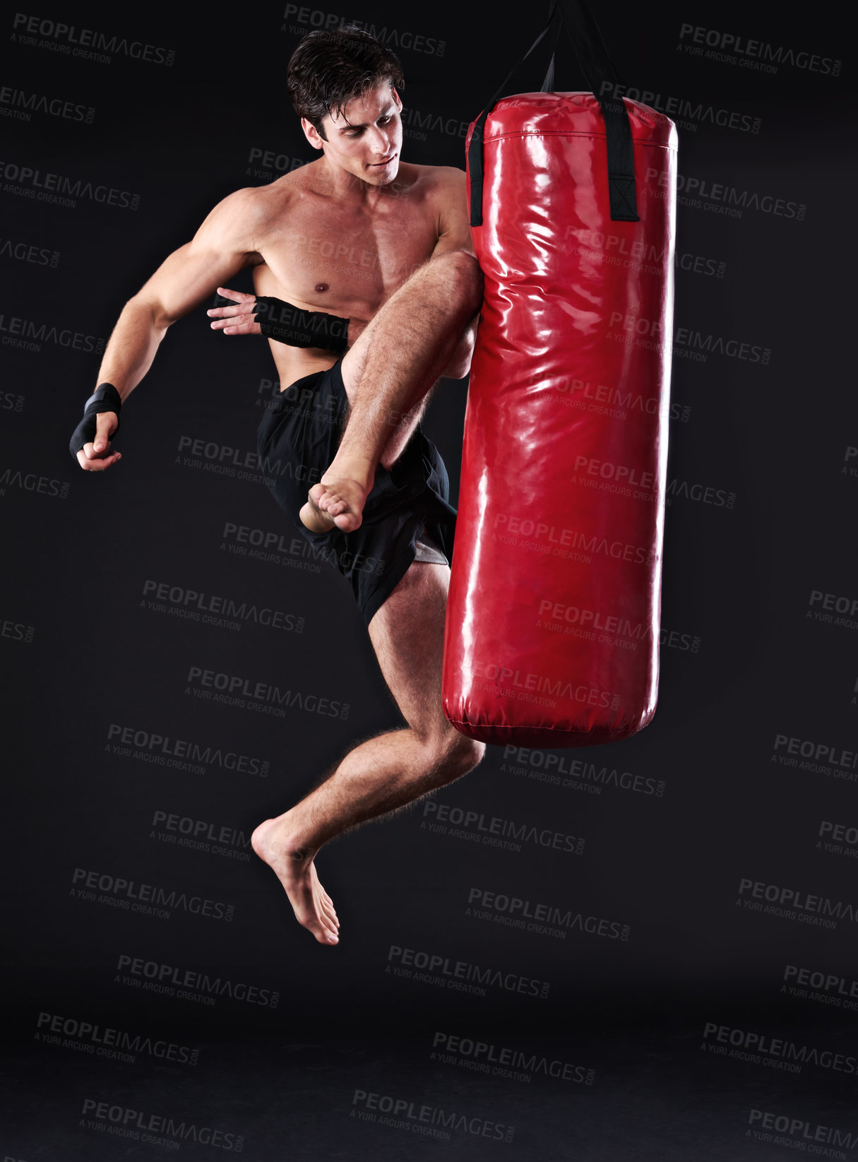 Buy stock photo Martial arts, man and training with knee in punching bag for skill development in dark studio with power. Male person, figure and black background in gym for fitness, muay thai jump and strength