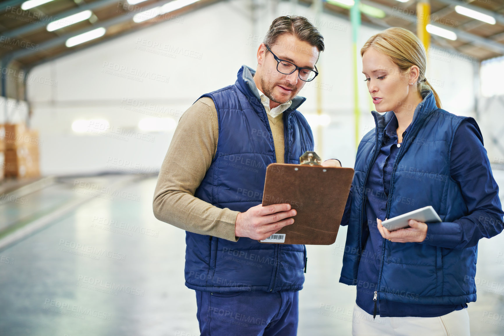 Buy stock photo Shot of two coworkers talking while standing in a large warehouse