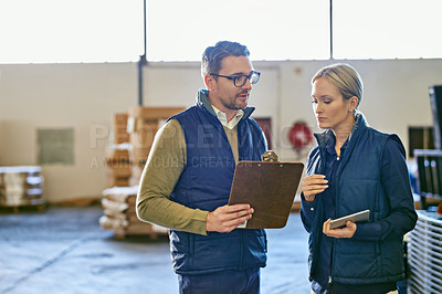 Buy stock photo Shot of two people looking at paperwork while working in a warehouse