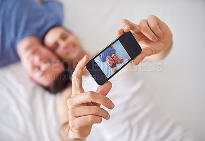 Buy stock photo Shot of a young gay couple taking a selfie while relaxing in bed