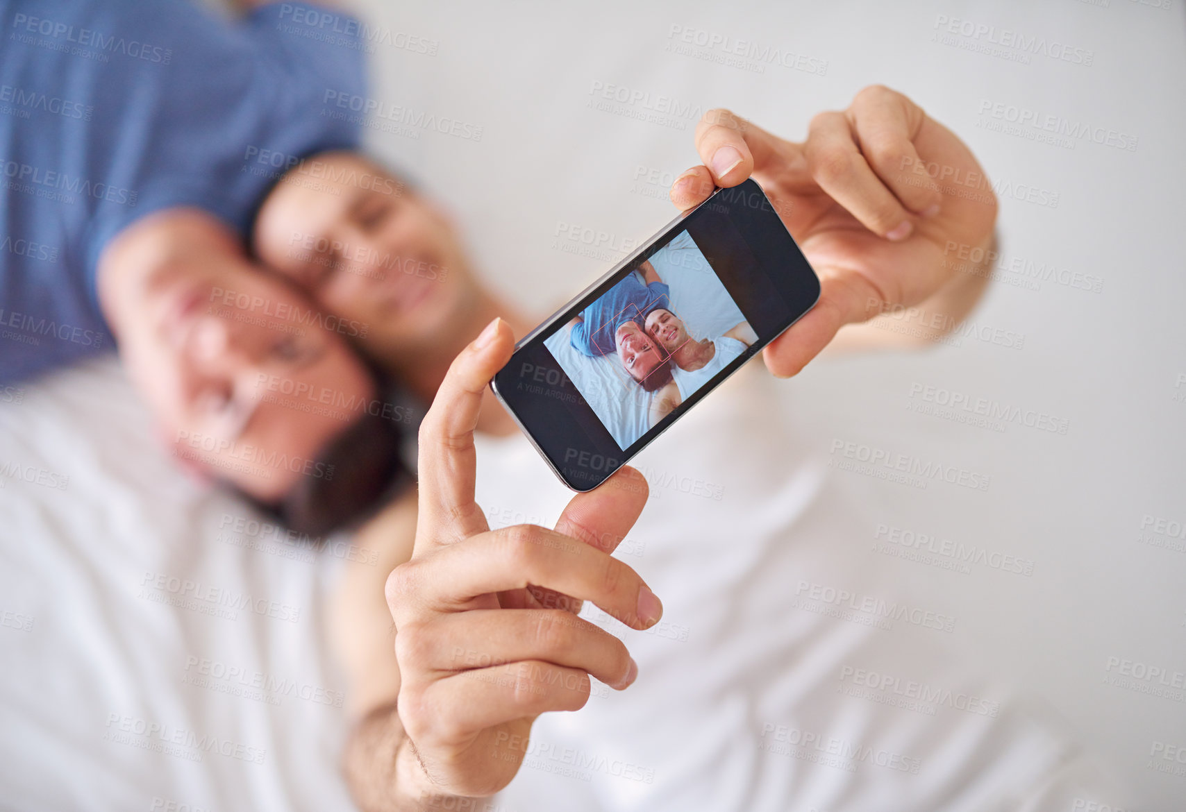 Buy stock photo Shot of a young gay couple taking a selfie while relaxing in bed