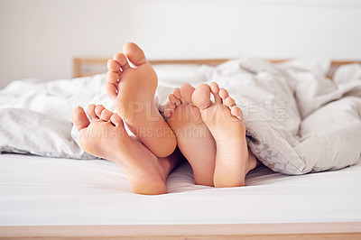 Buy stock photo Shot of a couple's feet poking out from under a duvet