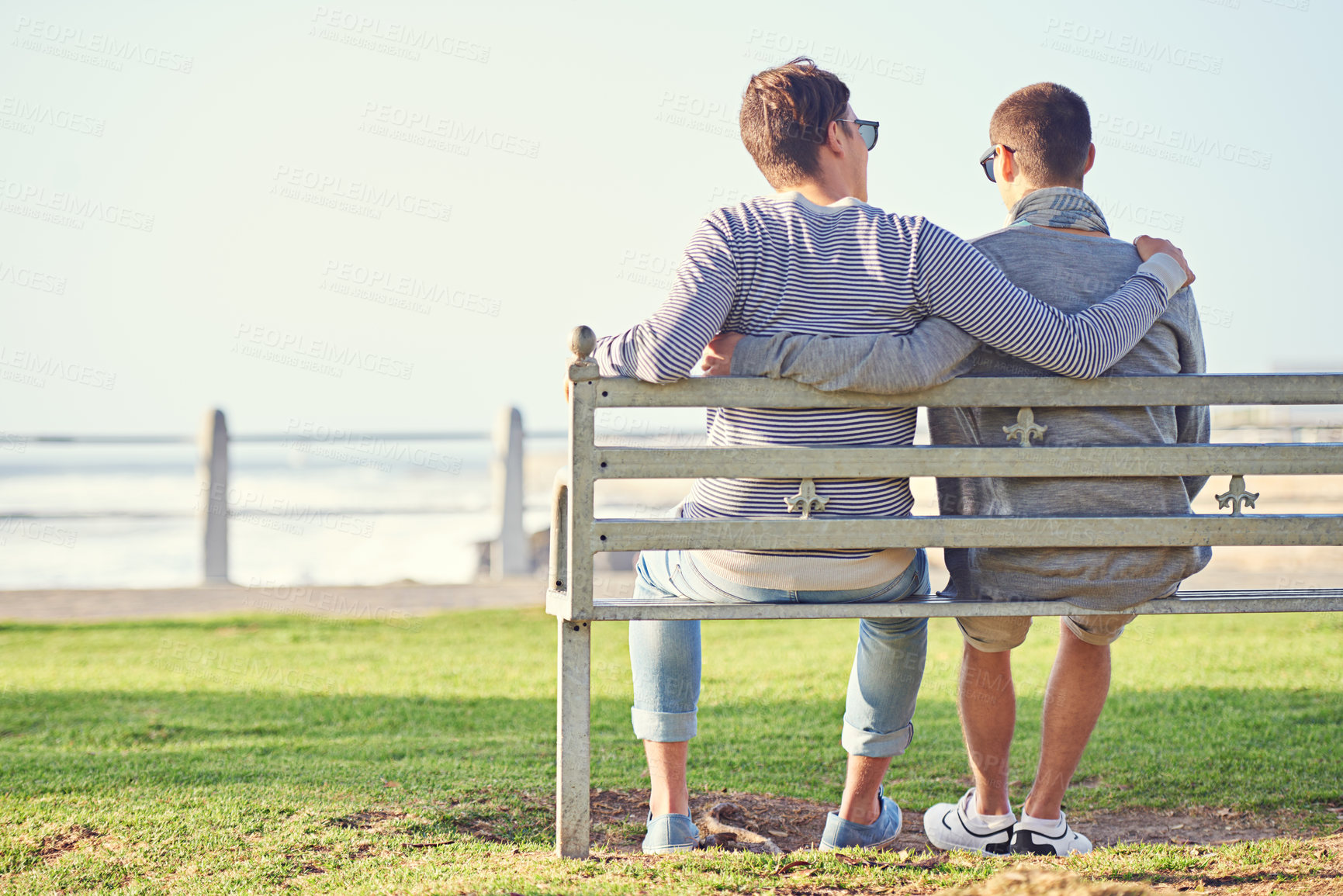 Buy stock photo Couple, park and bench for gay male people, ocean and promenade in nature. LGBT, love and hug or affection for married queer relationship, partner and honeymoon on holiday for bonding or relax