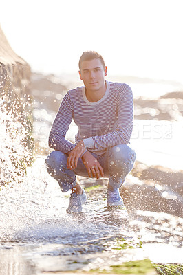 Buy stock photo Ocean, water and portrait of male man, sunset and nature for vacation or holiday. Confidence, splash and wave from beach on rocky terrain while travel, seaside and sunlight on coastline getaway