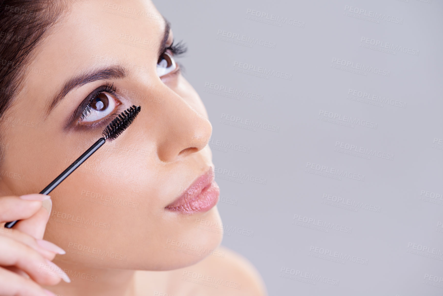 Buy stock photo Studio portrait of an attractive young woman applying mascara to her eyelashes