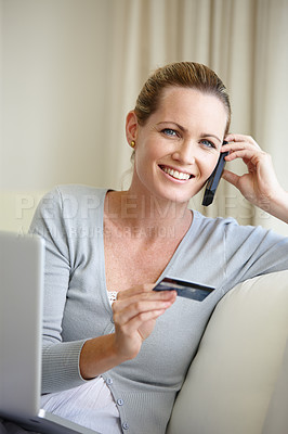 Buy stock photo A young woman talking on her cellphone while holding a bank card and sitting with a laptop