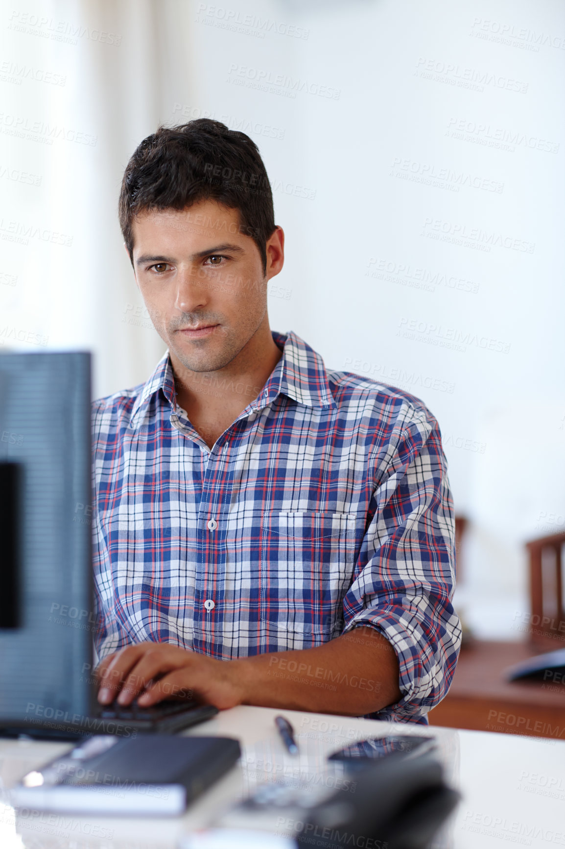 Buy stock photo A young man concentrating while sitting at a desk in front of a computer