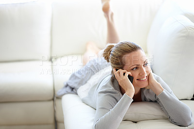 Buy stock photo One happy woman using her smartphone while lying on a couch with her feet up. Happy female making a phone call in her sunny living room apartment. Young adult enjoying her casual weekend at home