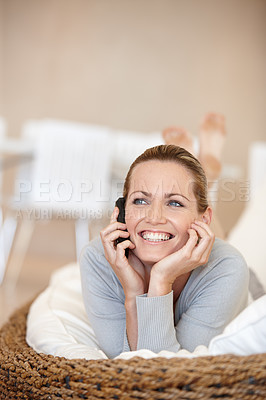 Buy stock photo Happy young woman thinking on a call on her phone while lying on a couch in the lounge at home. One cheerful female looking thoughtful while talking on a cellphone and relaxing in the living room