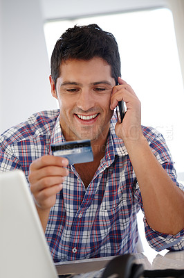 Buy stock photo Shot of a smiling man on the phone holding up a credit card while sitting at his desk
