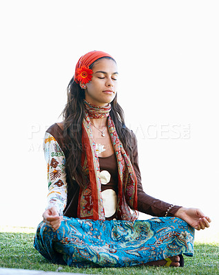 Buy stock photo Carefree hippie concentrating on her meditation while sitting outside on grass. Gypsy woman with flower in hair sitting alone and meditating with her legs crossed and eyes closed in lotus position