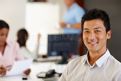 Buy stock photo Shot of a young businessman smiling at the camera with colleagues in the background