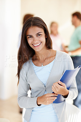 Buy stock photo Portrait of a happy latin young college student standing in a hallway or passage and holding documents. Intelligent university scholar on her way to a lecture class on campus to further her education