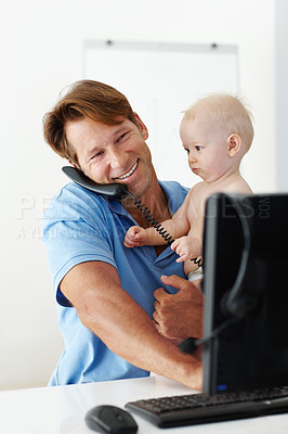 Buy stock photo Shot of a father at his desk holding a small child while talking on the phone
