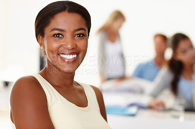 Buy stock photo Portrait of creative businesswoman sitting in the office with her colleagues in the background. Smiling entrepreneur and designer feeling confident in workplace. Black professional feeling successful