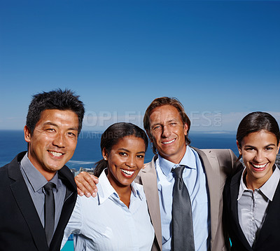 Buy stock photo Shot of four business people smiling in the sun with the ocean behind them