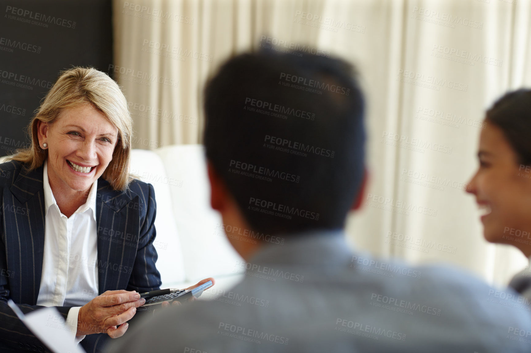 Buy stock photo Shot of a smiling woman using a calculator in a seated meeting