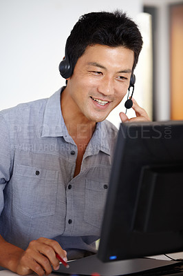 Buy stock photo Shot of an Asian man using a computer and talking on a headset